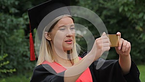 Beautiful girl in academic dress filming friends on smartphone, happy graduation