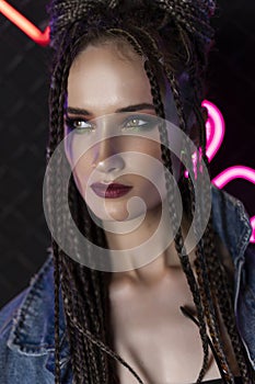 Beautiful girl with a afro cornrows, wearing denim jacket, sits on the floor in a night club at the wall made of rabitz net,