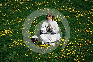 Beautiful girl astronaut without a helmet sits on a green lawn among flowers in a meditative position