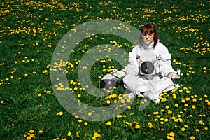 Beautiful girl astronaut without a helmet sits on a green lawn among flowers in a meditative position