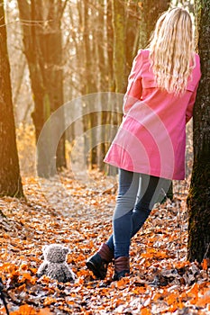 Beautiful girl in autumn forest stand back near tree and looking on sunlight