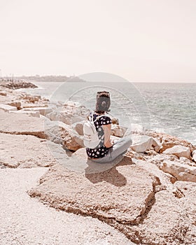 Beautiful girl with backpack sitting on stones near the sea.