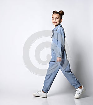beautiful girl with a bagel hairstyle walking in a blue cotton summer jumpsuit with comfortable pockets. on a light