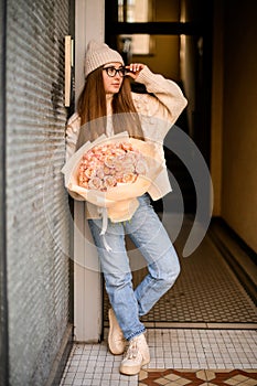 Beautiful girl in beige sports shoes standing near a wall with a chic roses