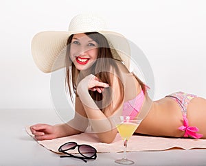 Beautiful girl in bikini, sunglasses and a big hat lying on the beach towel standing beside a glass of cocktail