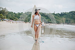 beautiful girl in bikini with surfboard standing on beach