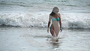 Beautiful girl in bikini walks out from ocean after swimming to the tropical beach. Young woman in swimsuit goes out