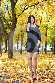 Beautiful girl in black dress and red shoes in yellow city park, fall season