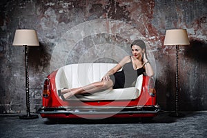 A beautiful girl in a black dress is sitting on an unusual handmade sofa. Sofa from the car seat.