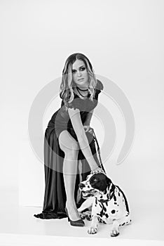 Beautiful girl in a black dress on a white background with a dalmatian dog