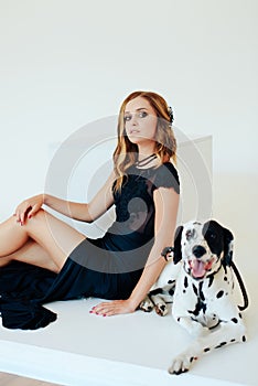 Beautiful girl in a black dress on a white background with a dalmatian dog