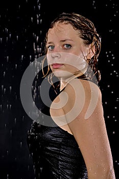 A beautiful girl in a black T-shirt stands under drops of water.