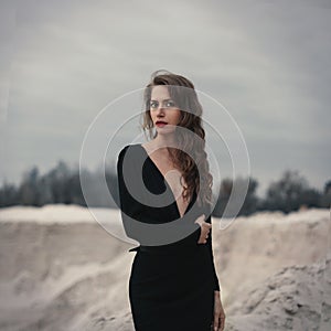 Beautiful girl in in black vintage dress with curly hair posing on the sand. Woman in retro dres. Worried sensual emotion . Retro