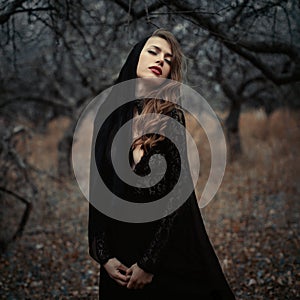 Beautiful girl in in black vintage dress with curly hair posing in the woods. Woman in retro dress lost in the forest. Worried sen