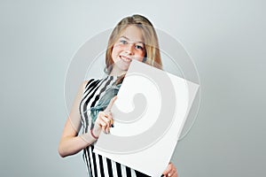 Beautiful girl with blank canvas board smiling on grey background.