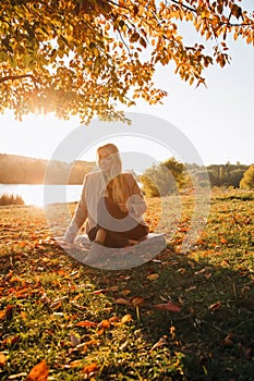 Beautiful girl with blond hair in autumn landscape at sunset. Portrait of a girl sitting on the grass, selective focus