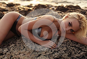 Beautiful girl with blond hair in bikini posing at sunset beach