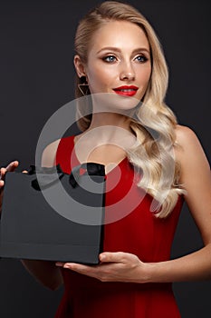 Beautiful girl with blond hair, classic make-up in a elegant red dress and shopping bag. Beauty face.