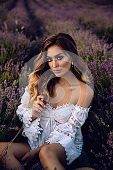 Beautiful girl with blond hair in elegant clothes posing in summer flowering lavender field