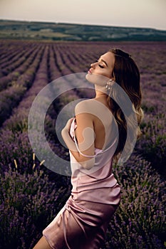 Beautiful girl with blond hair in elegant clothes posing in summer flowering lavender field