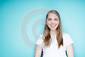A beautiful girl with blond hair and a white T-shirt is smiling. Isolated on blue background photo