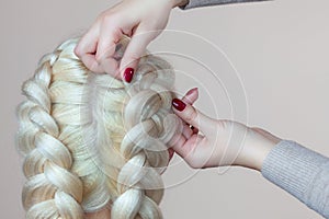 Beautiful girl with blonde hair, hairdresser weaves a braid close-up, in a beauty salon.