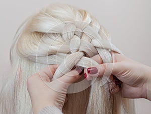 Beautiful girl with blonde hair, hairdresser weaves a braid close-up, in a beauty salon