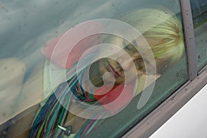 Beautiful girl with blonde hair taking a nap in the car on a rainy day photo