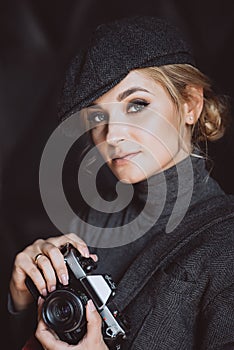 Beautiful girl blonde photographer in a strict suit and a cappie is holding an old retro camera in her hands