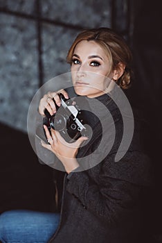 Beautiful girl blonde photographer in a strict suit holds in his hands the old retro camera