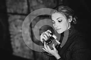Beautiful girl blonde photographer in a strict suit holds in his hands the old retro camera. Black and white photo