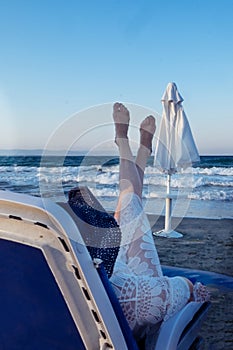 A beautiful girl in a blue bikini and a white hat is sunbathing on the beach, lying on a white chaise longue