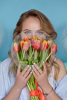 Beautiful girl in the blue dress with flowers tulips in hands on a light background