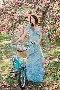 Beautiful girl in blue dress walk with bicycle in blooming spring garden