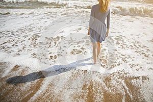 Beautiful girl in blue dress is walking on the beach. Amazing summer photo. Woman near the sea. Holiday travel concept. Slim legs