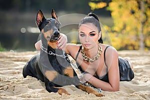 Beautiful girl with blue eyes posing with a doberman lying on the sand