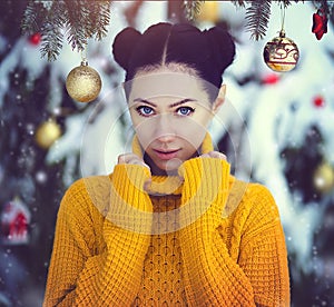 Beautiful girl with blue eyes in a yellow sweater under a snow-covered Christmas tree with Christmas toys. A girl in