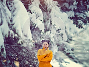 Beautiful girl with blue eyes in a yellow sweater under a snow-covered tree. A girl in a fairy magical winter forest.