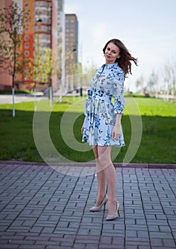 The beautiful girl in a blue short dress costs against the background of the street per windy sunny day