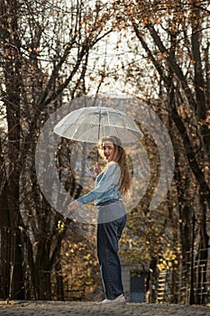 Beautiful girl in blue sweater with transparent umbrella on autumn alley. Young woman in autumn park