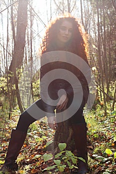 Beautiful girl in boots and jacket sitting on tree stump