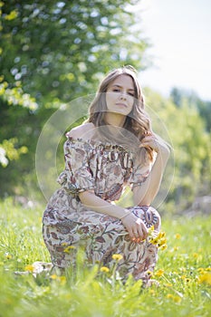 A beautiful girl with a bouquet of first flowers straightens her hair sitting on the lawn of the Park