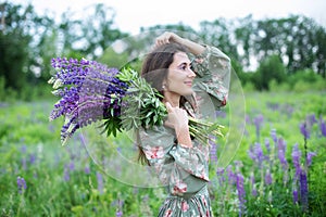 Beautiful girl with a bouquet of wild flowers. A girl in dress with a bouquet of lupine stands in flower field. Summertime. Bloomi