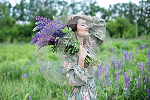 Beautiful girl with a bouquet of wild flowers. A woman in dress with a bouquet of lupine stands in flower field. Summertime. Bloom