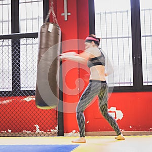 Beautiful girl boxing against punching bag (intentionally blurred)