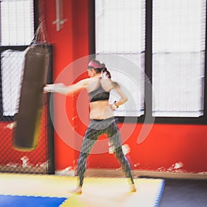 Beautiful girl boxing against punching bag (intentionally blurred)