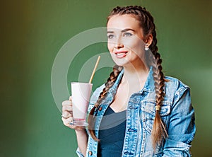 Beautiful girl with braids sitting in a cafe and drinking a milkshake, looking out the window