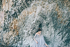 Beautiful girl bride in a long blue dress sitting near the cliff