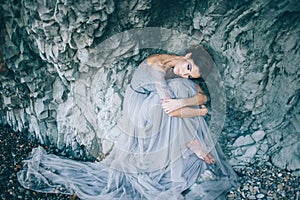 Beautiful girl bride in a long blue dress sitting near the cliff bowed his head