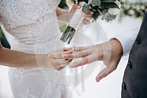 Beautiful girl bride in wedding white dress puts on the groom`s finger the wedding gold ring